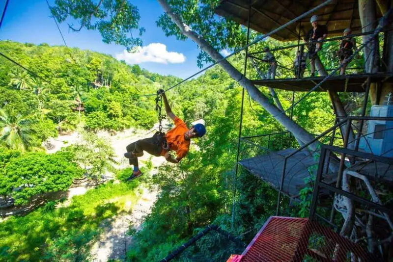 Zipline rider above the tropical valley near Wang Sai Waterfall